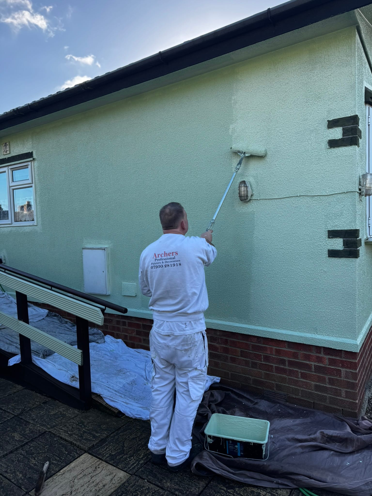 Archers decorator rolling fresh masonry paint onto a house exterior